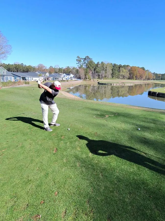 A golfer tees off beside the water on a course